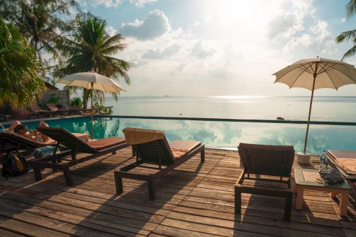 A serene beach scene with sun loungers, umbrellas, and a view of the ocean under a partly cloudy sky at sunset.